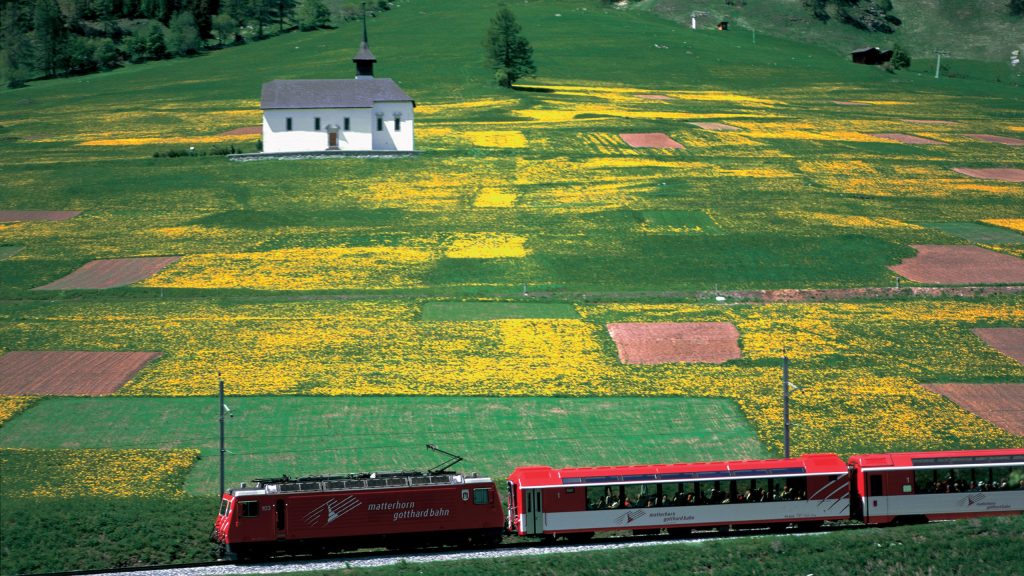 Switzerland. get natural. 
A train of the Matterhorn Gotthard Bahn (MGB) at Ritzingerfeld near Ritzingen in Goms valley, Canton Valais. In the background the Mother of God Chapel dated 1687.

Schweiz. ganz natuerlich.
Die Matterhorn Gotthard Bahn (MGB) im Ritzingerfeld bei Ritzingen im Goms, Kanton Wallis. Im Hintergrund die Muttergotteskapelle von 1687.

Suisse. tout naturellement. 
Un train du Matterhorn Gotthard Bahn (MGB) a Ritzingerfeld pres de Ritzingen dans la vallee de Conches, canton du Valais. La chapelle Mere de Dieu datant de 1687.

Copyright by: Switzerland Tourism   By-Line: swiss-image.ch/Christof Sonderegger