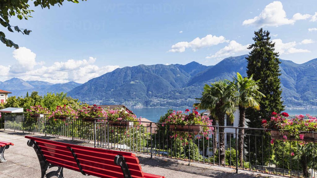 Switzerland, Ticino, Locarno, Park bench overlooking Lake Maggiore and surrounding mountains in summer